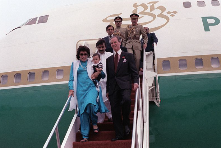 Bhutto embarking from an airplane at Andrews Air Force Base during her 1989 state visit to the United States. She carried her son; her husband followed behind.